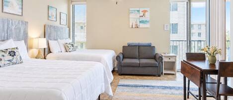 A hotel room with two beds, a sofa, a dining table, and a ceiling fan.