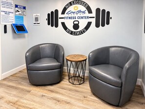 Un gimnasio con dos sillones de cuero, una pequeña mesa de madera y una pared con el logotipo y las normas del gimnasio.