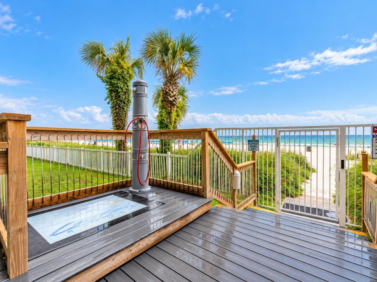 A wooden deck with a metal railing, a water feature, and a view of the beach.