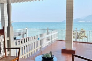 A balcony with a view of the sea, wooden furniture, and a railing. - Kela Coast Seaside Inn (Shenzhen)