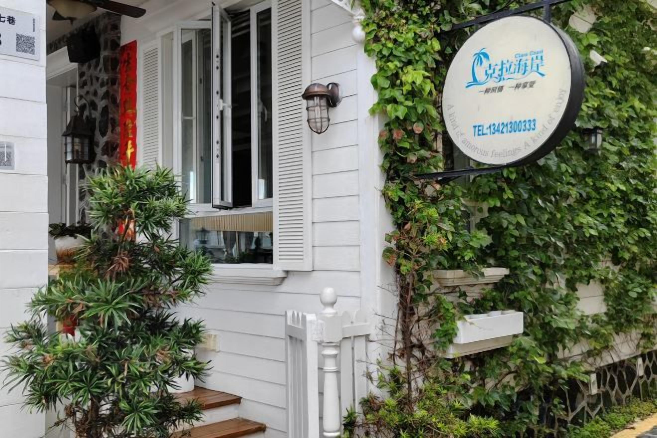 A house with a white exterior, a visible staircase, a potted plant, and a sign with contact information.