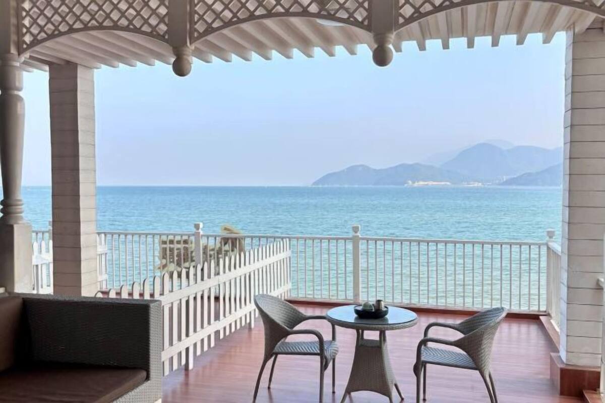 A balcony with a view of the sea, a white railing, and wicker furniture.