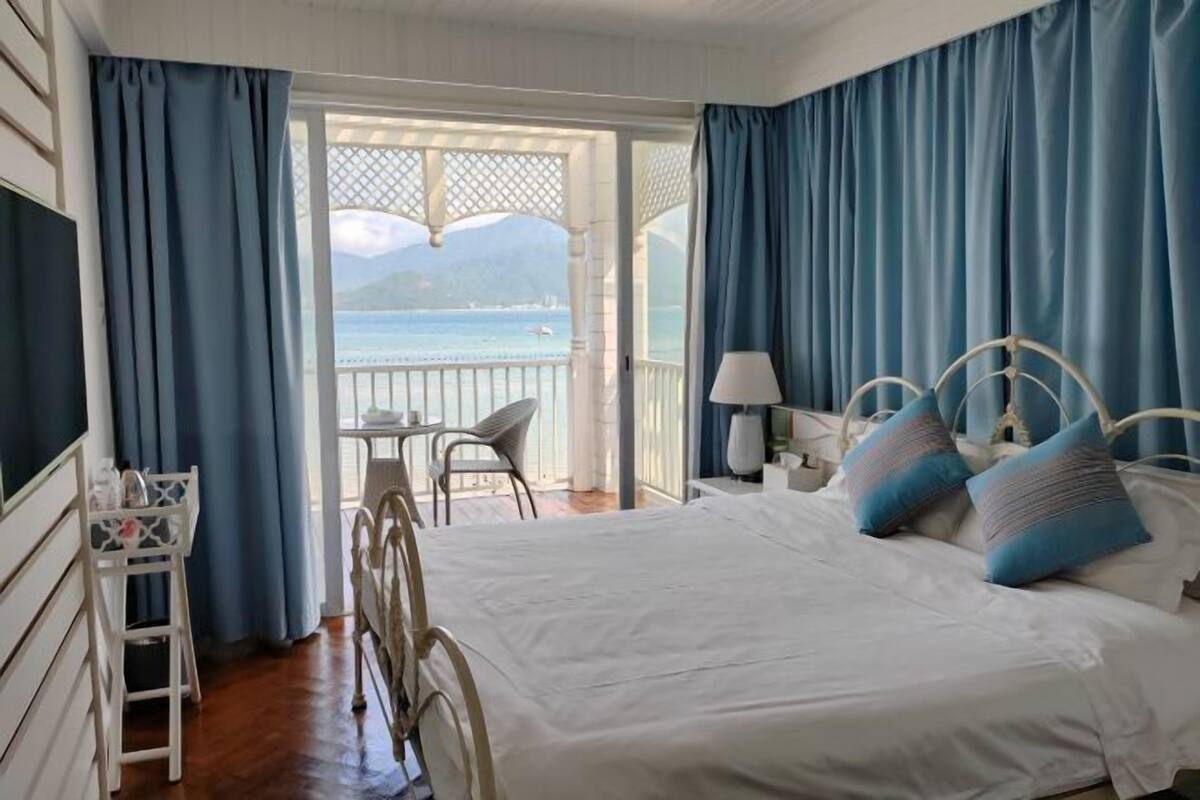 A bedroom with a bed, a chair, a table, and a view of the sea.