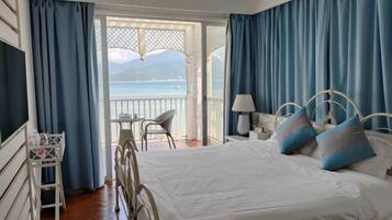 A bedroom with a bed, a chair, a table, and a view of the sea.