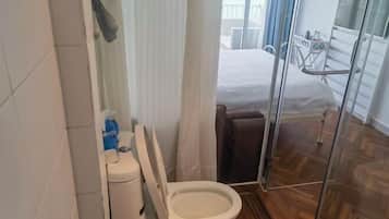 Un baño con inodoro, ducha y puerta de vidrio que da a un balcón.