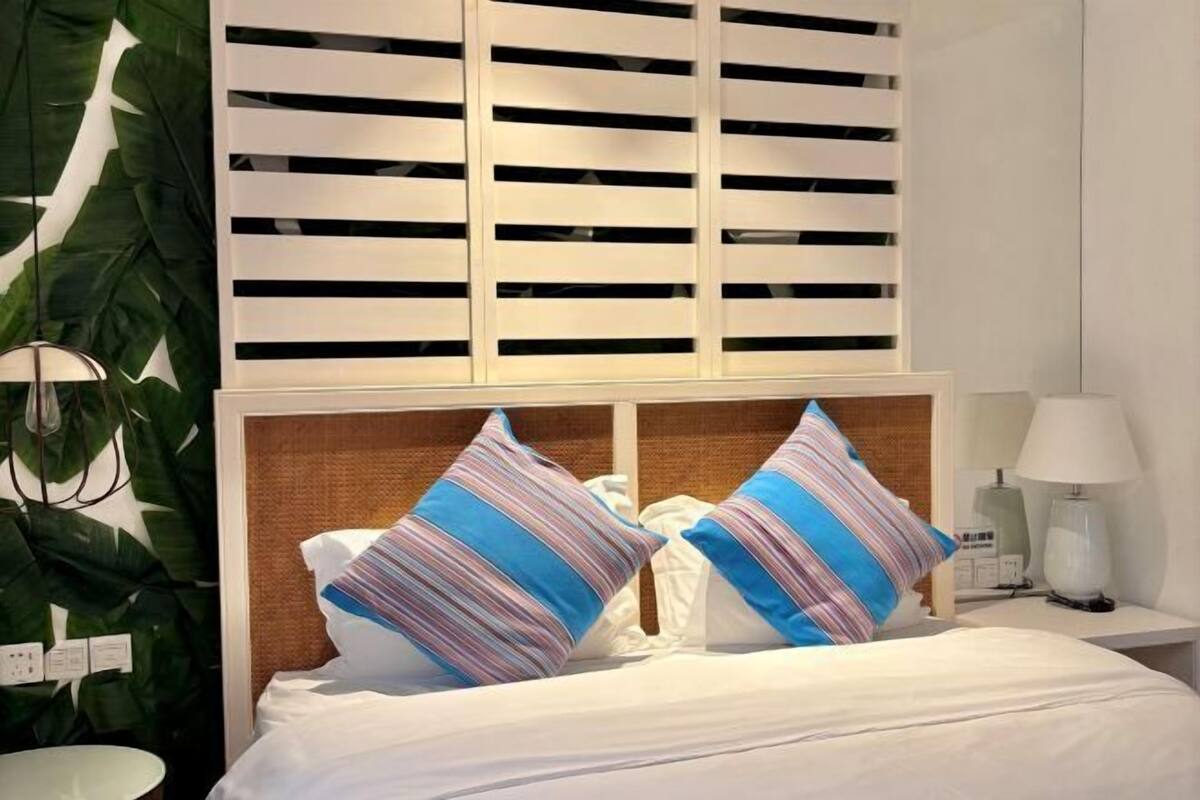 A hotel room with a bed, a nightstand, a lamp, and a wall with a window blind.