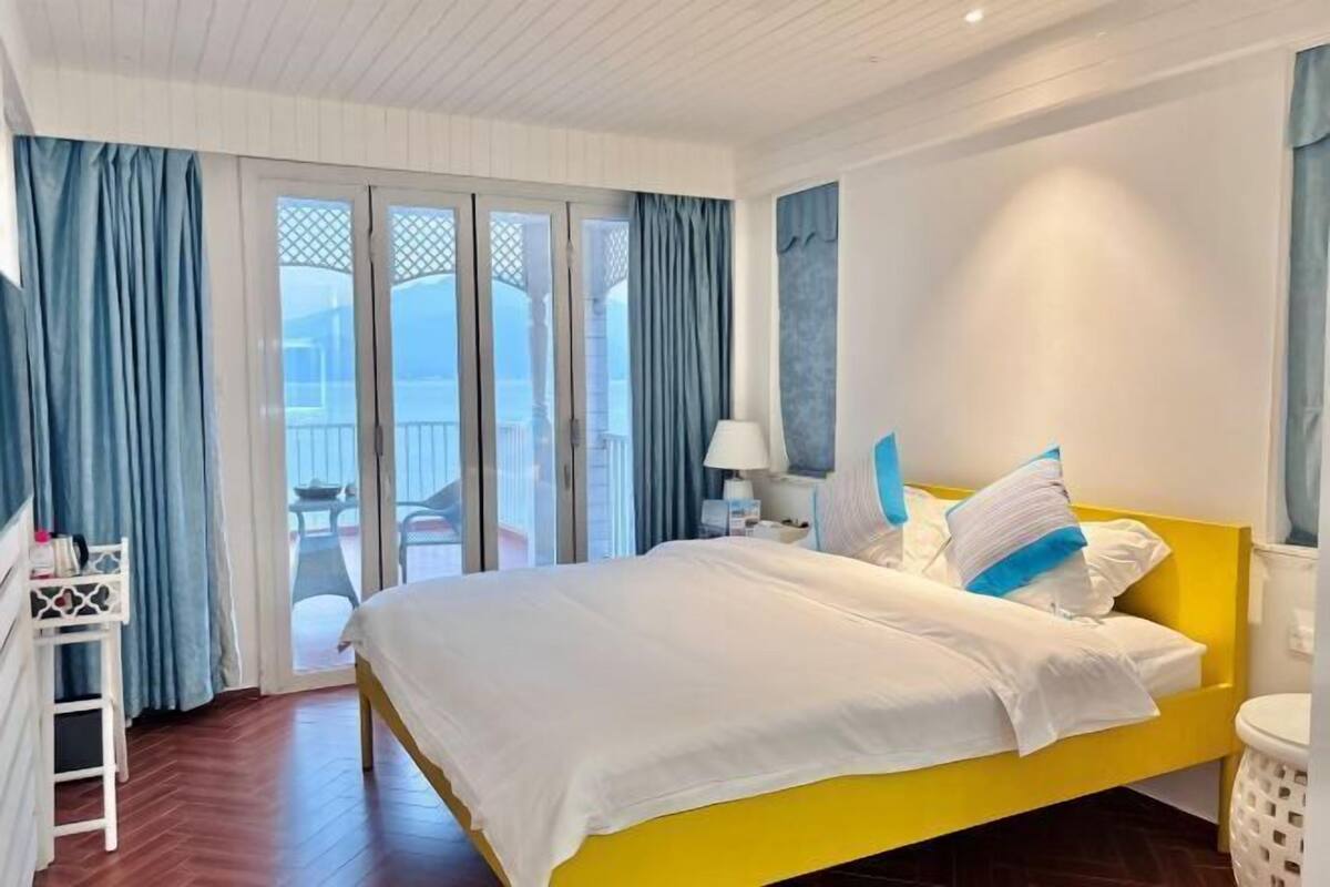 A hotel room with a bed, a nightstand, a lamp, a white cabinet, and a view of the outside.