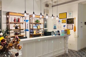 Zona de recepción con mostrador blanco, lámparas colgantes y estantes con diversos objetos.
