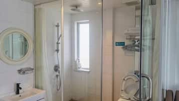 Un baño moderno con ducha envuelta en vidrio, inodoro y lavamanos con espejo.
