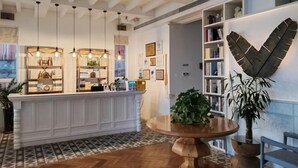 A reception area with a white counter, pendant lighting, a large wooden table, and a bookshelf with various items. - Kela Coast Seaside Inn (Shenzhen)