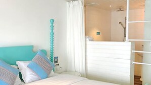 A bedroom with a bed, pillows, a white headboard, a bathroom with a shower, and a white cabinet. - Kela Coast Seaside Inn (Shenzhen)