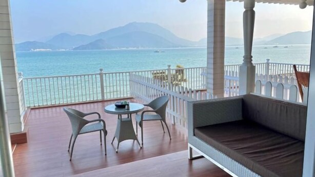 A balcony with a view of the sea, a round table, two chairs, and a cushioned bench. - Kela Coast Seaside Inn (Shenzhen)