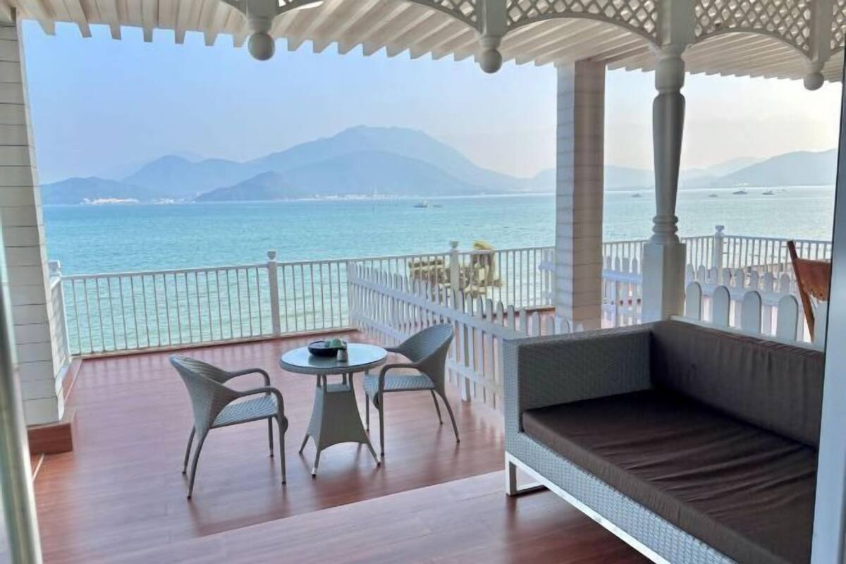 A balcony with a view of the sea, a round table, two chairs, and a cushioned bench.