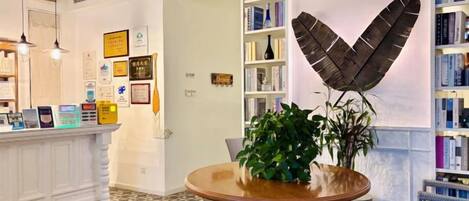 A reception area with a round wooden table, a potted plant, and a bookshelf.
