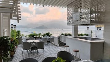 Una terraza con asientos al aire libre, vista al mar y una estructura blanca decorativa.