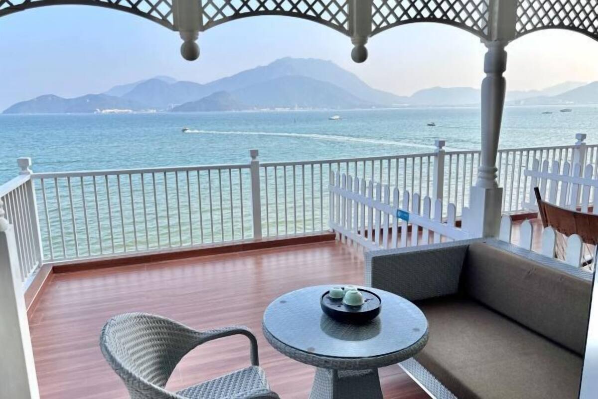 A balcony with a view of the sea, a wicker chair, a small round table, and a white fence.