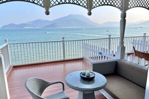 A balcony with a view of the sea, a wicker chair, a small round table, and a white fence. - Kela Coast Seaside Inn (Shenzhen)