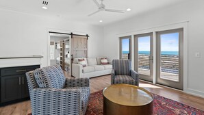 A modern living room with a sofa, two patterned armchairs, a coffee table, and a view of the ocean through large windows. - Costa-Florida: 7 Bedrooms, Private Pool, Community Pool and Gym (Mexico Beach)