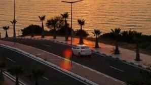 Un coucher de soleil sur une étendue d’eau, avec une route et des palmiers au premier plan.