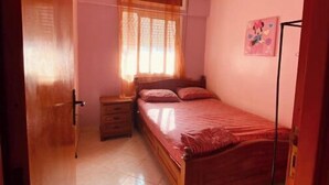 Une chambre à coucher avec un lit en bois, une table de chevet, une commode, une fenêtre avec des rideaux et un ventilateur de plafond.