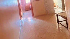 Un couloir avec un sol carrelé, un miroir accroché au mur et une porte donnant sur une autre pièce.