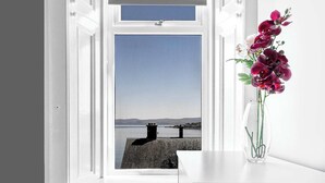 Una habitación con ventana que da a un cuerpo de agua, un escritorio blanco y un jarrón con flores.