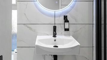A bathroom with a white marble sink, a round mirror with underglow lighting, and a black door.