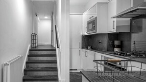 Una cocina moderna con estufa a gas, electrodomésticos de acero inoxidable y una escalera que sube a otro nivel.