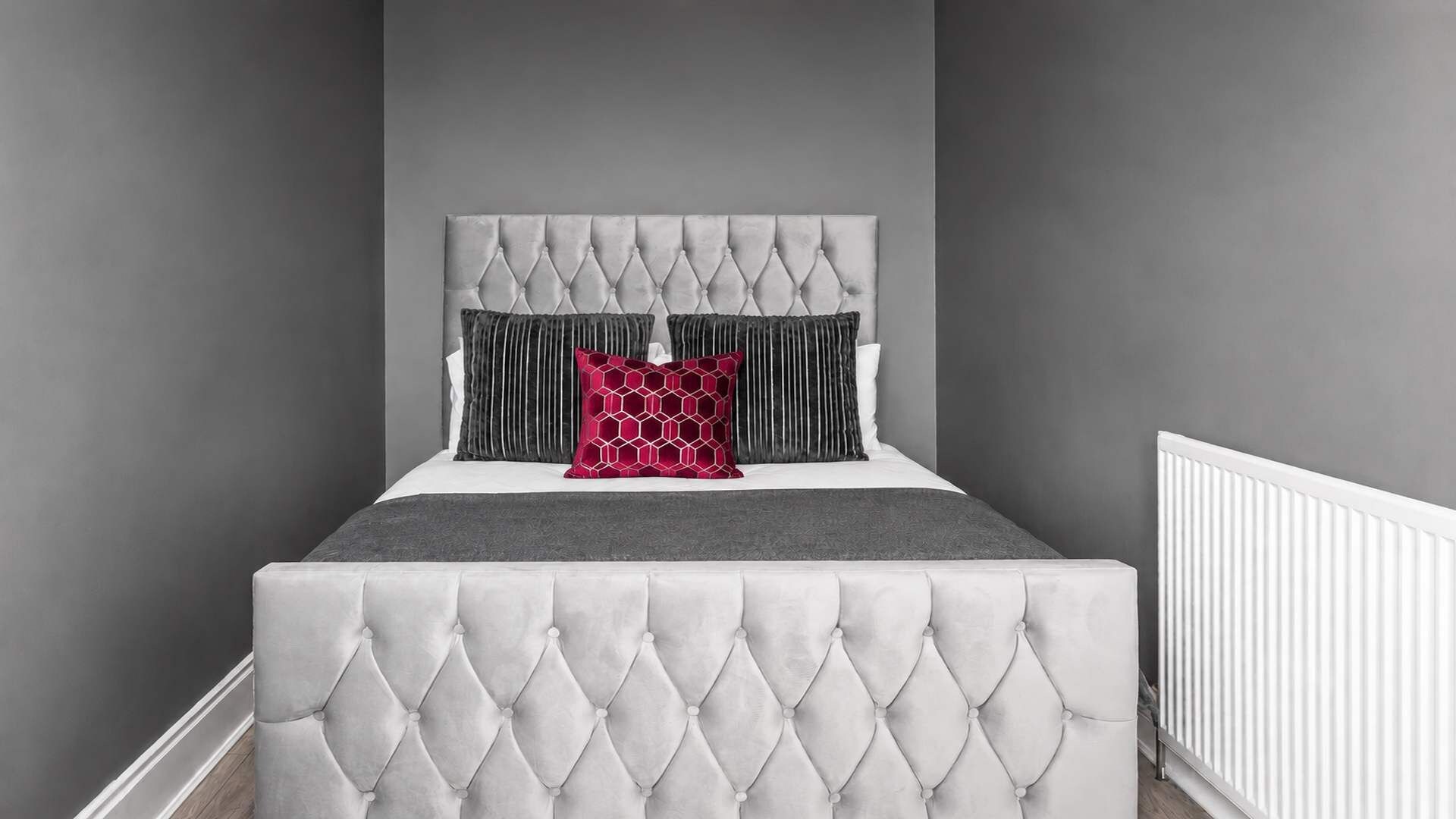 A bedroom with a tufted headboard, a grey bedspread, and two pillows.