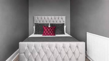 A bedroom with a tufted headboard, a grey bedspread, and two pillows.