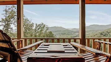 Une terrasse en bois avec une table et des chaises, offrant une vue sur un paysage montagneux.