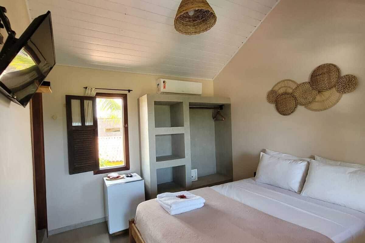 Ein Schlafzimmer mit Bett, Kleiderschrank, kleinem Tisch, Pendelleuchte und einem Fenster mit Rollläden.