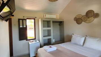 A bedroom with a bed, a wardrobe, a small table, a hanging light fixture, and a window with shutters.