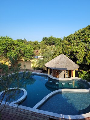 A pool area with a thatched-roof structure, surrounded by lush greenery and a clear blue sky. - Pousada Oceano Caraiva (Porto Seguro)