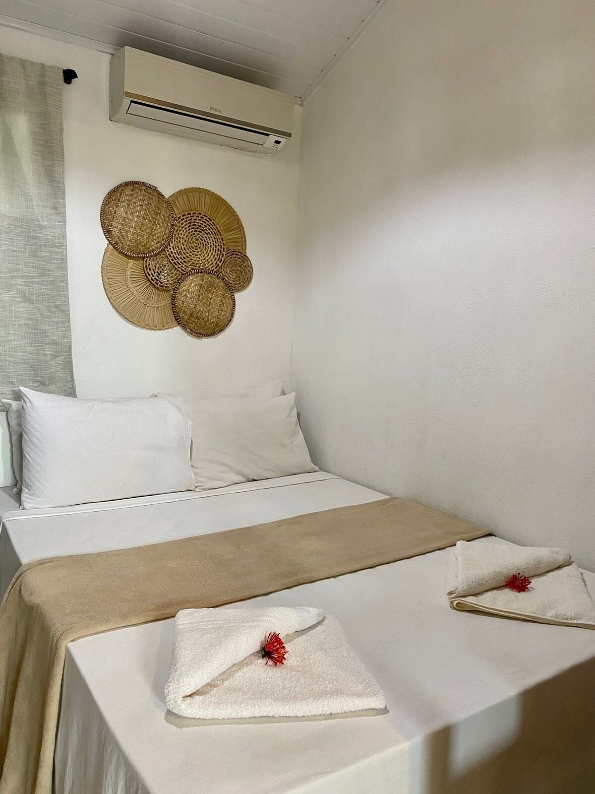 Quarto de hotel com cama, ar condicionado fixado na parede e um painel decorativo de tecido.