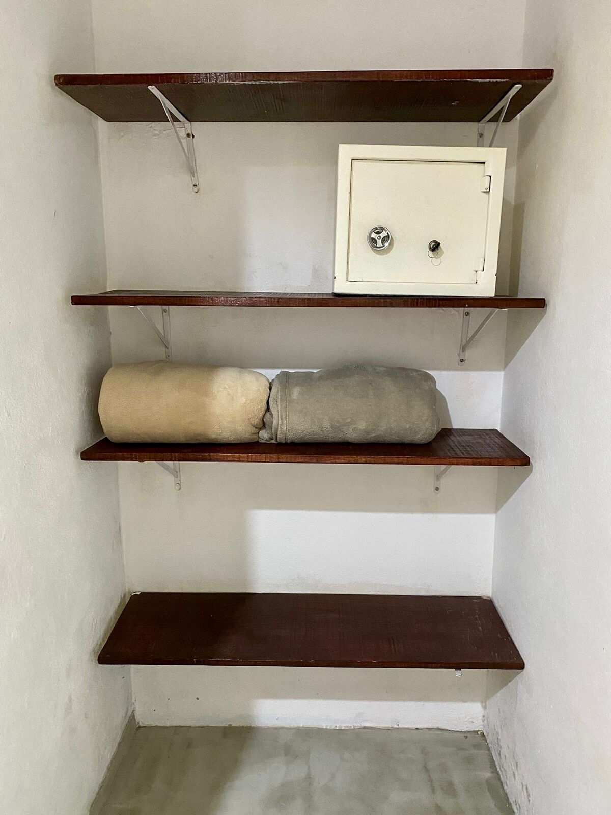 A corner with three wooden shelves, one of which holds a beige and gray object.
