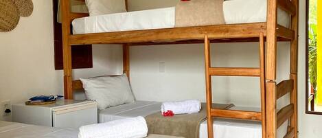 A bunk bed room with a ceiling fan, a small table with a bag, and a woven basket on the wall.