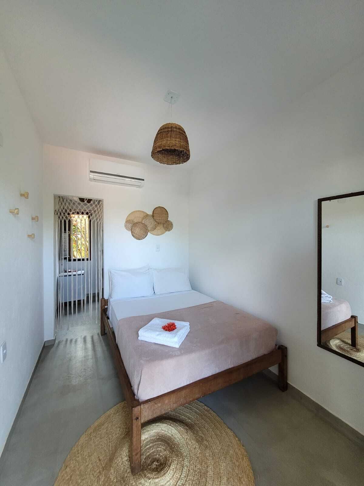 A bedroom with a wooden bed, a woven ceiling light, a wall-mounted air conditioner, and a mirror reflecting part of the room.