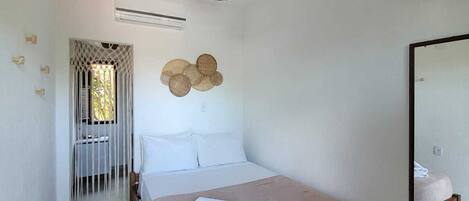 A bedroom with a wooden bed, a woven ceiling light, a wall-mounted air conditioner, and a mirror reflecting part of the room.