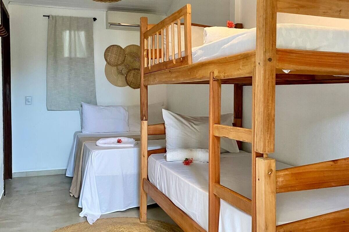 Ein Stockbett mit weißer Bettwäsche, ein kleiner Tisch mit weißem Tuch und eine gewebte Matte auf dem Boden.
