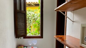 A compact room with a small white refrigerator, a wooden bench, a window with open shutters, and a wooden shelf. - Pousada Oceano Caraiva (Porto Seguro)