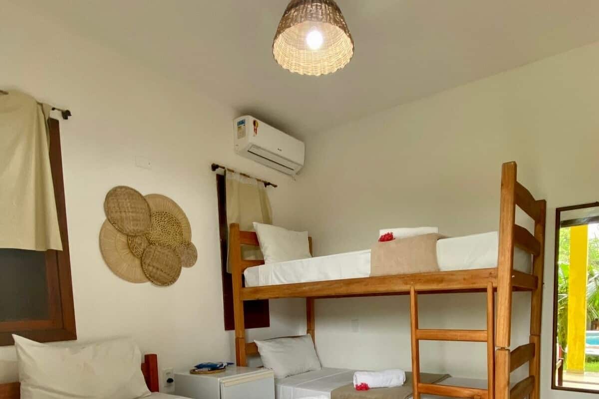 Ein Zimmer mit Etagenbetten, einem Deckenventilator, einer Klimaanlage und einer gewebten Matte auf dem Boden.
