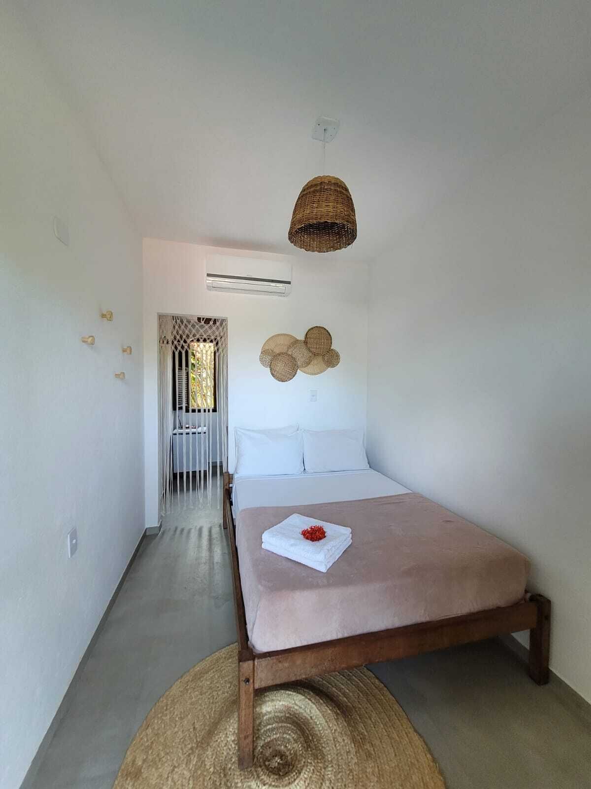 A modern bedroom with a wooden bed, a woven pendant light, a wall-mounted air conditioner, and a decorative wall piece.