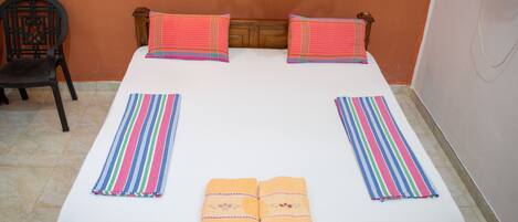 Una cama con dos almohadas, una funda a rayas y dos toallas dobladas.