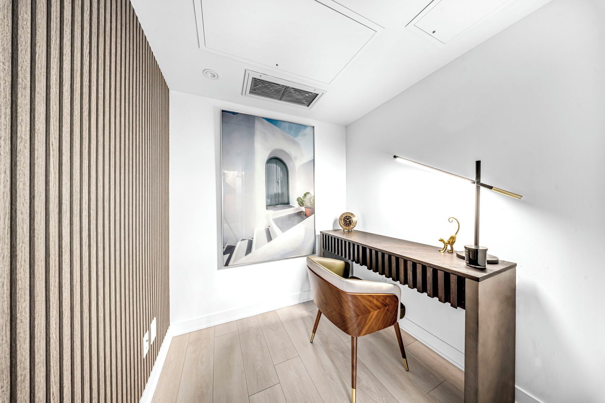 Una habitación moderna con pared de listones de madera, un cuadro grande enmarco, una consola elegante con lámpara y una silla con detalle dorado.