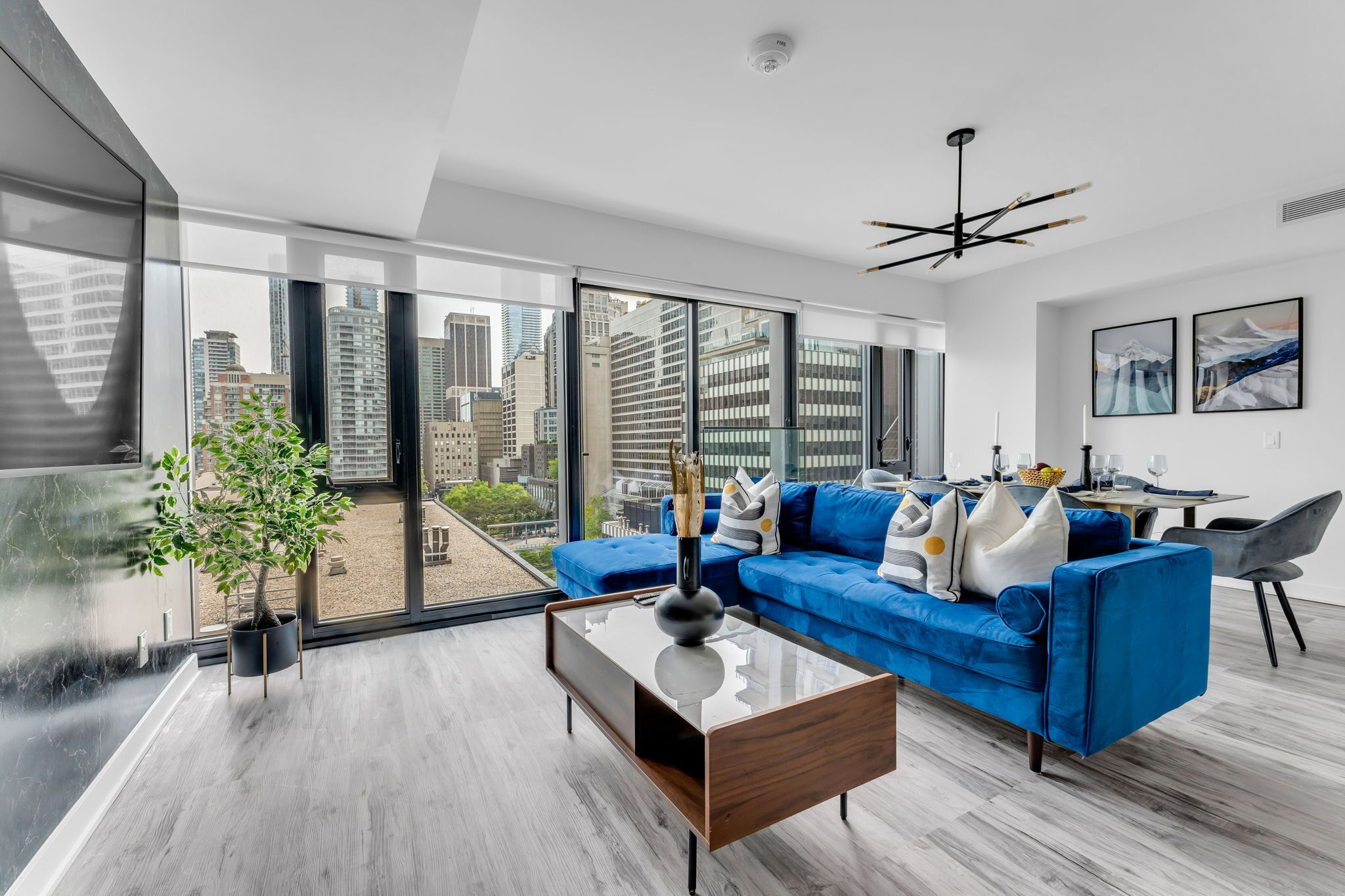 A modern living room with a blue sofa, a glass coffee table, and a city view through large windows.