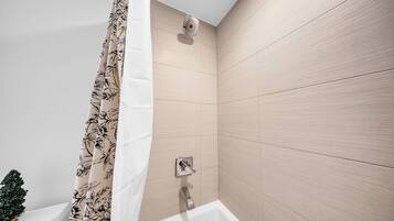 A modern bathroom with a shower, a toilet, and a small decorative tree.