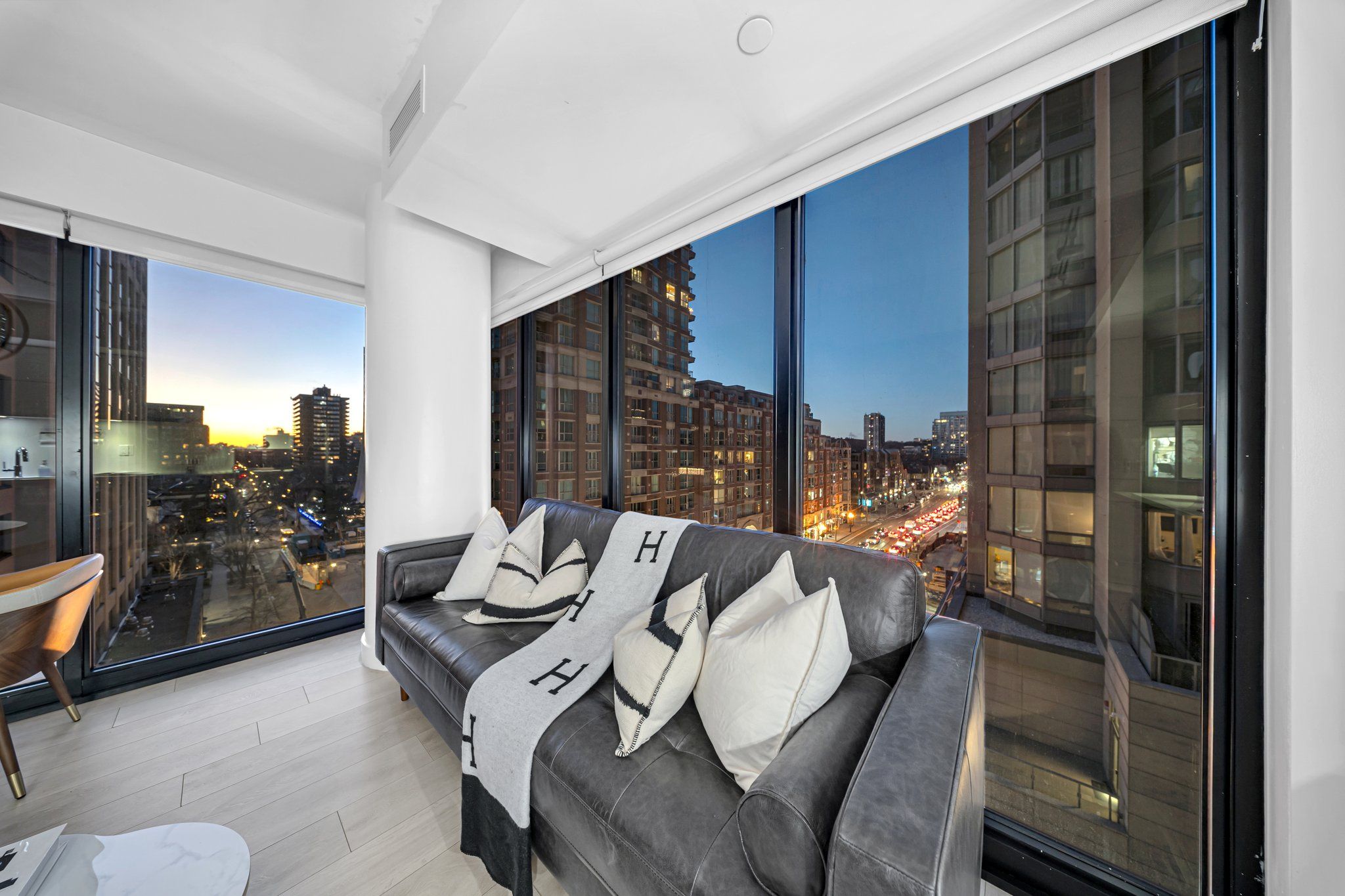 Ein modernes Wohnzimmer mit einem großen Fenster, das auf eine städtische Skyline bei Dämmerung blickt.