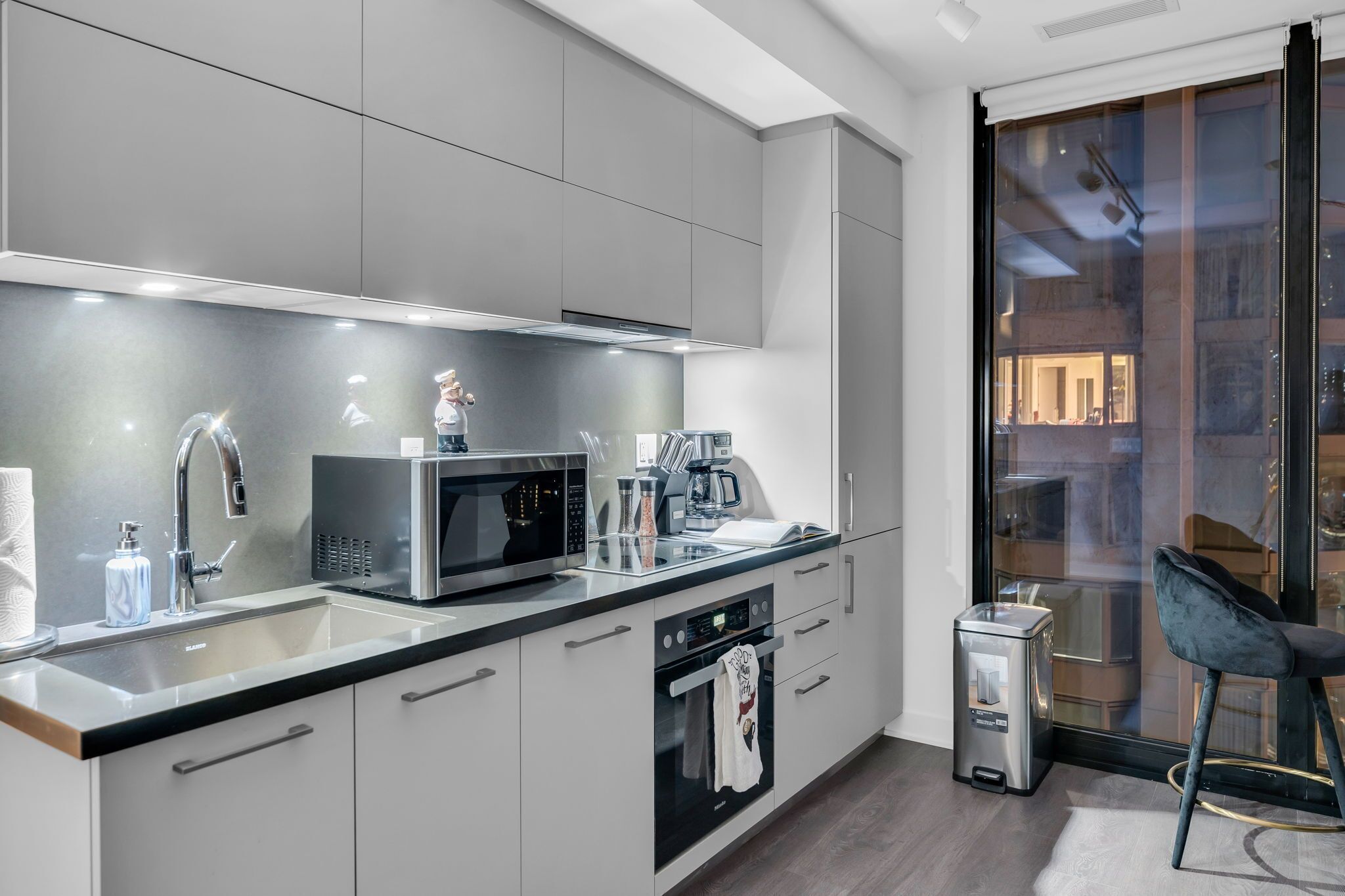 A modern kitchen with stainless steel appliances, a built-in oven, and a large window offering a view of the city.
