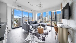 A modern living room with a gray sofa, a round wooden coffee table, and a glass dining table.